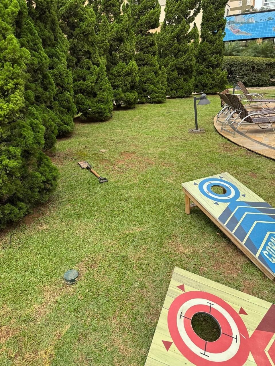 Gramado aparado com fileira de tuias e área de lazer ao fundo