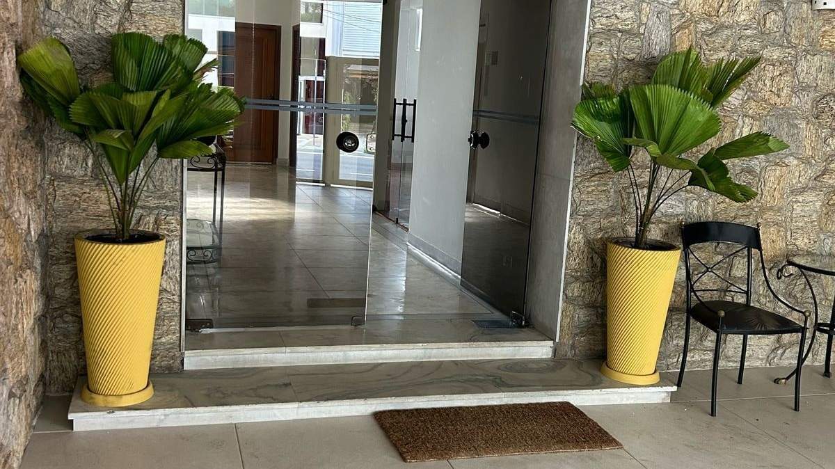 Entrada de prédio com dois vasos amarelos de palmeira-leque