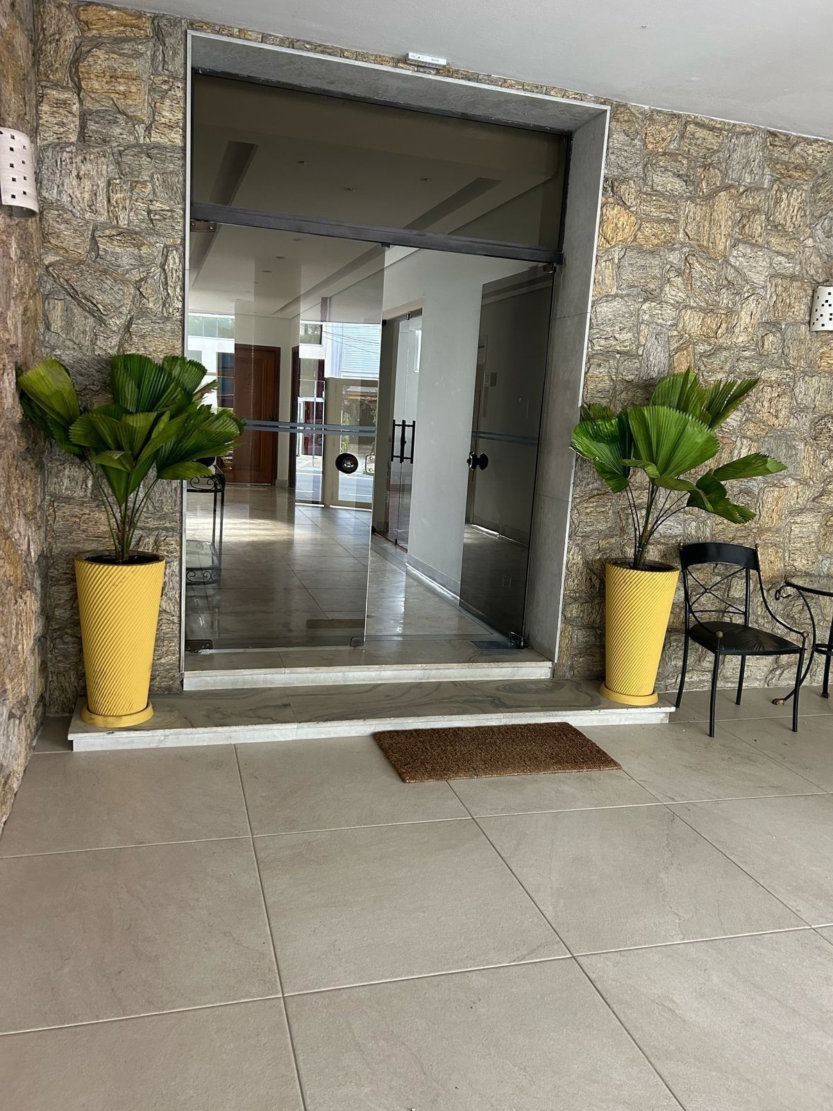 Entrada de prédio com dois vasos amarelos de palmeira-leque