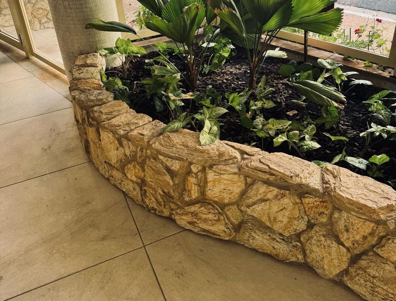 Jardineira de pedra com palmeira-leque e folhagens no hall envidraçado de um prédio