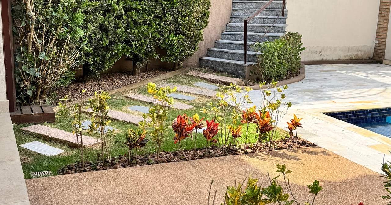 Jardim de casa com canteiros de plantas coloridas, cerca-viva no muro e escada até a piscina