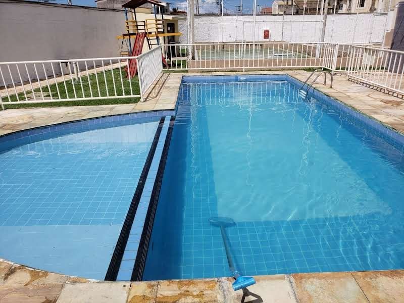 Piscina de condomínio com a vara de limpeza encostada na borda, água limpa e azul