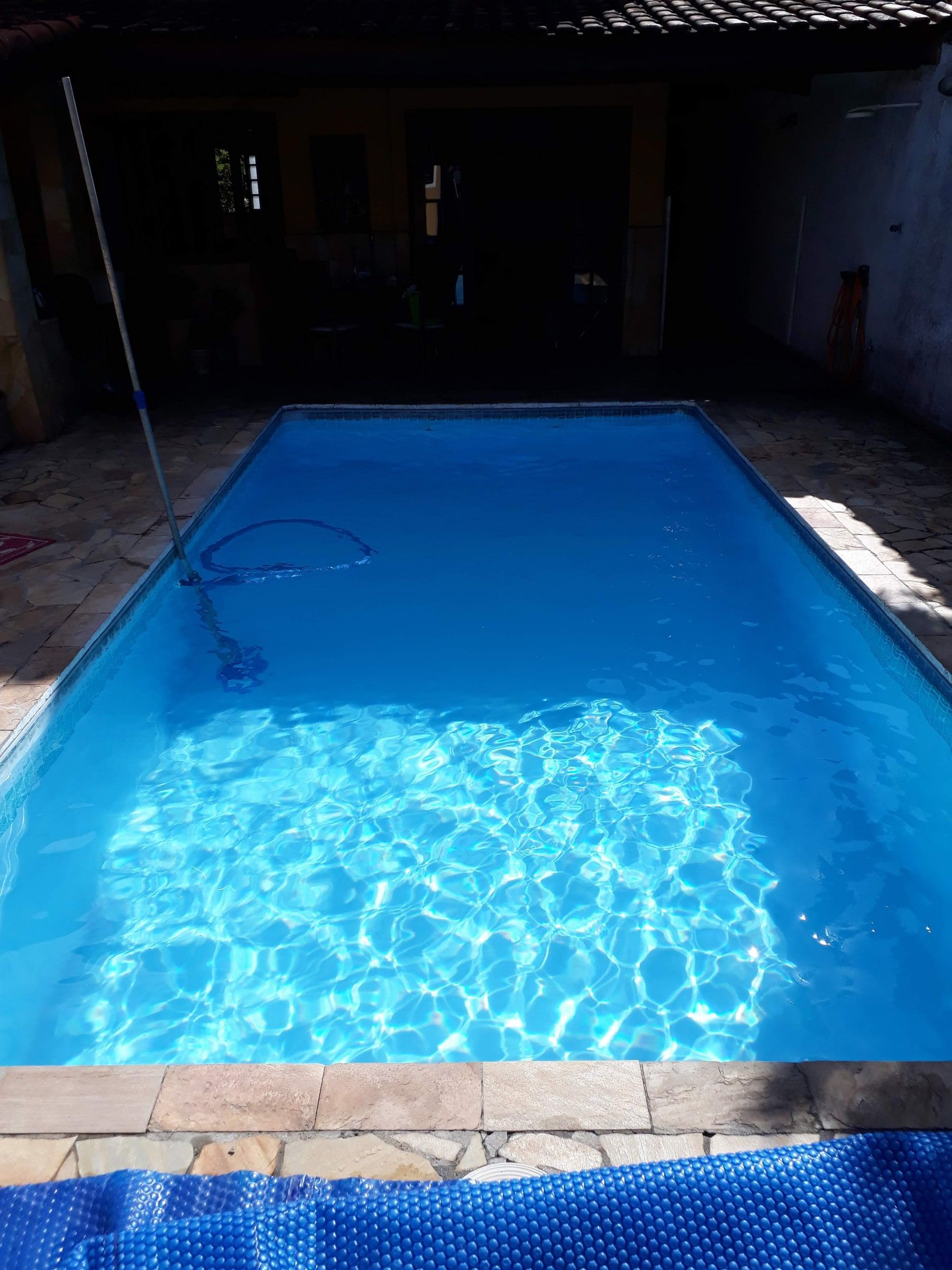 Piscina de casa com água azul e transparente, com o aspirador e a mangueira no fundo durante a limpeza