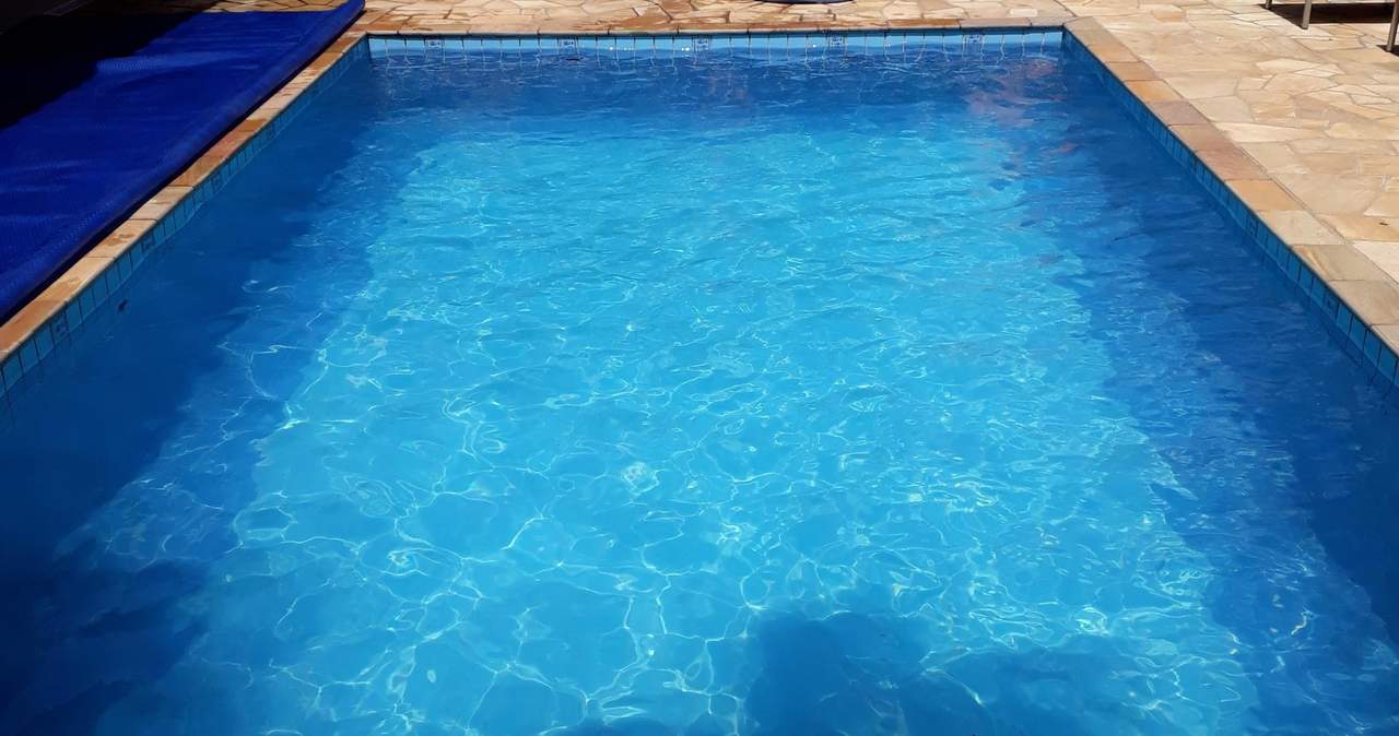Piscina de casa com água azul e limpa, deck e pergola de madeira ao lado